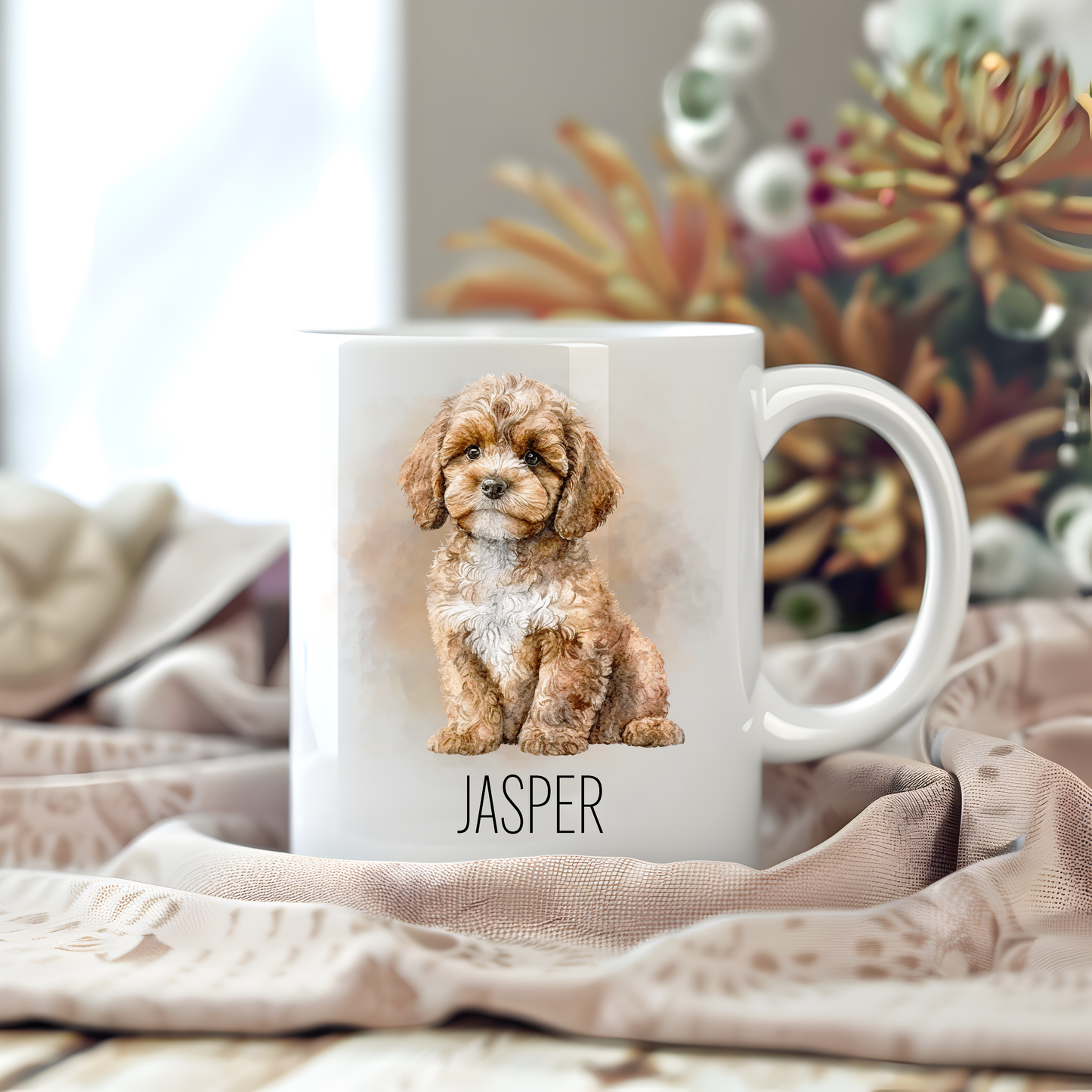 Personalised coffee mug featuring a seated Cavapoo position on a white ceramic mug which has been placed on a beige cloth.  Stems of large  flowers accessorizes the image.
