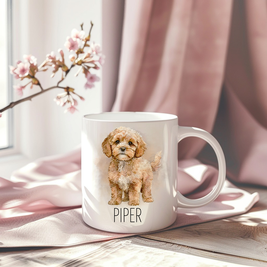 Cavapoo in a standing position on a white ceramic mug which has been placed on a pink drape.  A stem of small pink flowers accessorizes the image.