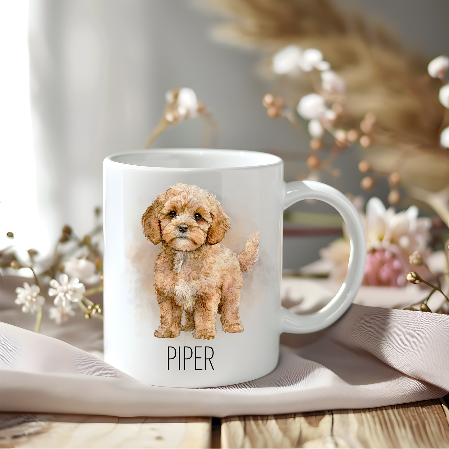 Cavapoo coffee mug personalised with a pet name.  The mug is sat on a wooden surface with a creamy coloured cloth and various flowers adorn the background.