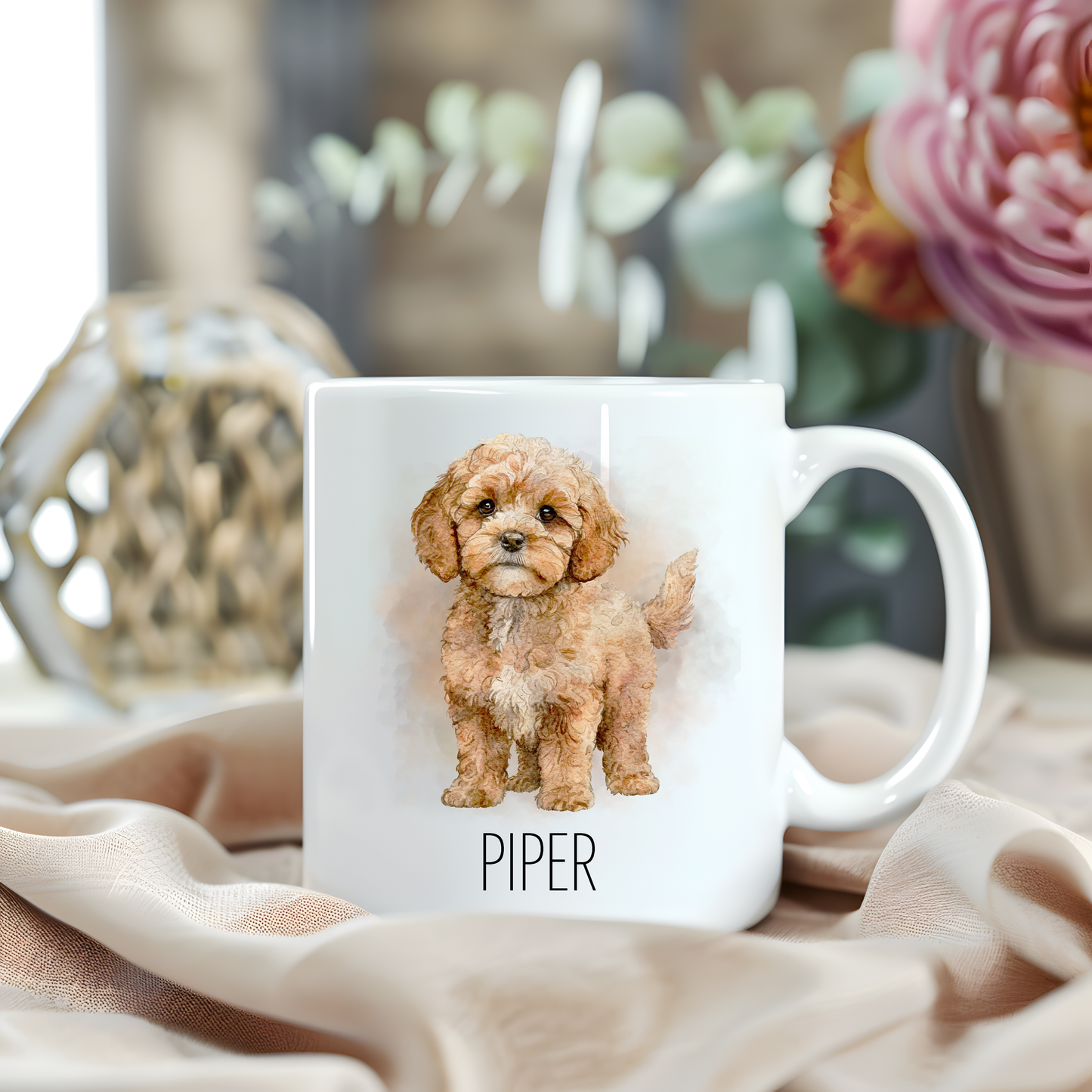 Personalised coffee mug featuring a seated Cavapoo dog on a white ceramic mug which has been placed on a beige cloth.  A large pink flower with green foliage accessorizes the image.