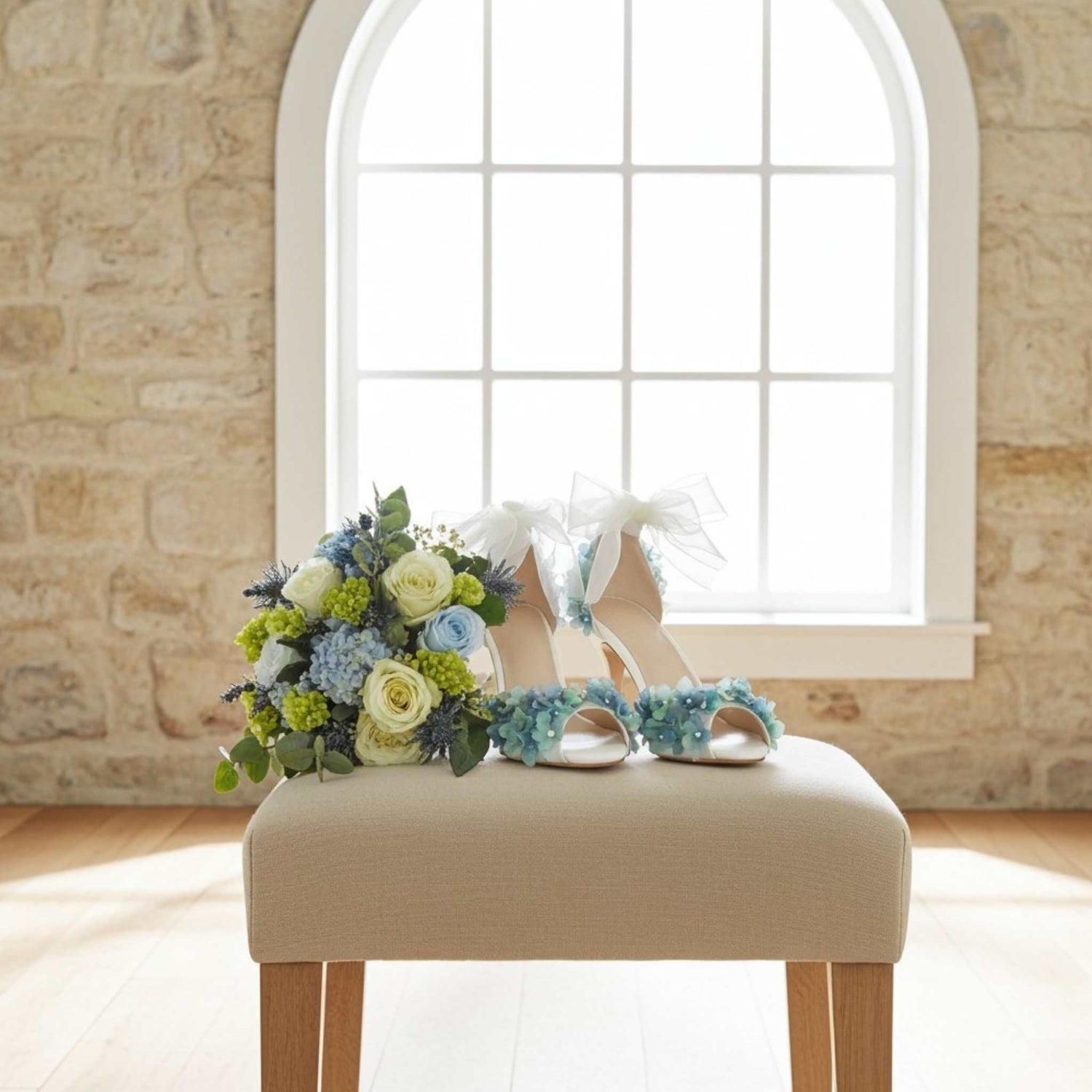 Bridal shoes with floral decorations on a stool in front of a window with stone walls.