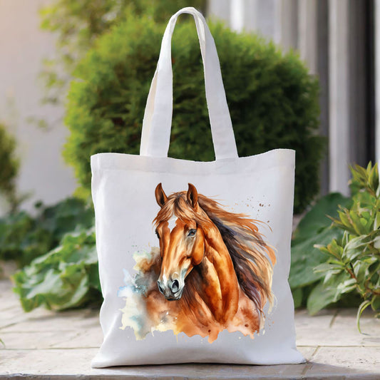 White tote bag with a long handle showing a chestnut horse head with long flowing mane. . The bag is placed in front of a large green shrub with green foliage to the right side.