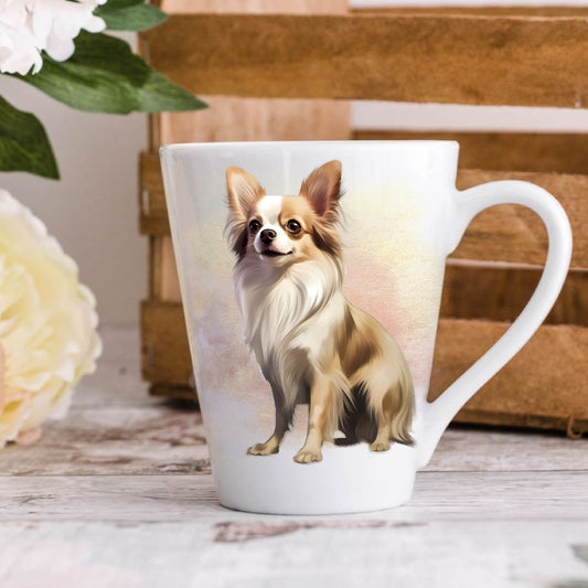 A white ceramic latte coffee mug with a colorful illustration of a Chihuahua dog on the front, displayed on a wooden surface with flowers and books in the background.