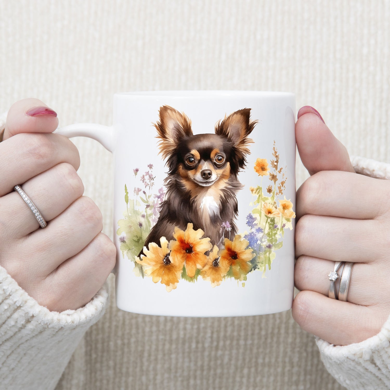 White 11oz ceramic mug has a vibrant printed image of a liver and tan long haired Chihuahua dog sat among flowers.  The mug is being held in a woman's hands.