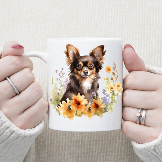 White 11oz ceramic mug has a vibrant printed image of a liver and tan long haired Chihuahua dog sat among flowers.  The mug is being held in a woman's hands.