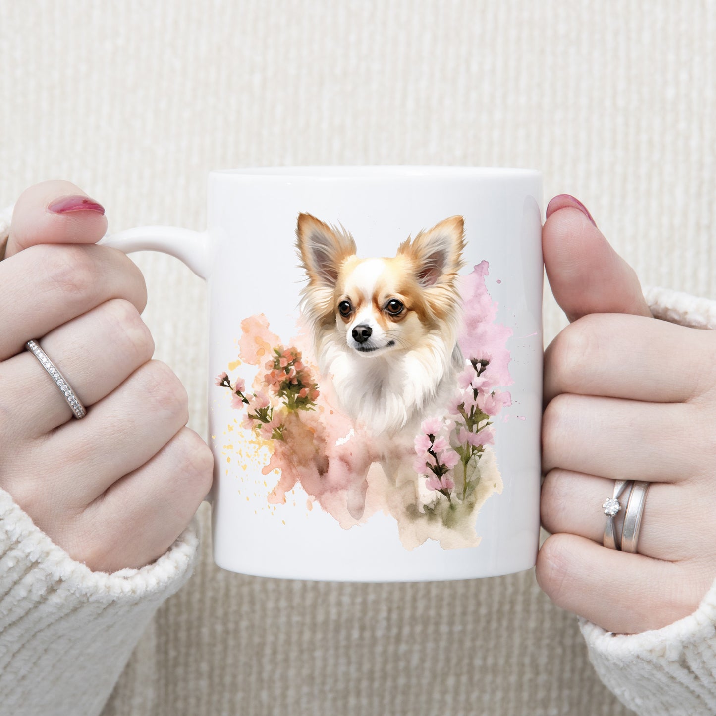 White 11oz ceramic mug has a vibrant printed image of a long haired Chihuahua dog sat among pink and peach flowers.  The mug is being held in a woman's hands.