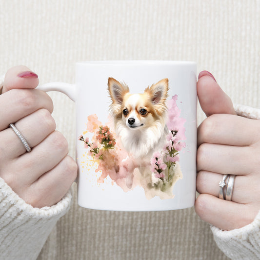 White 11oz ceramic mug has a vibrant printed image of a long haired Chihuahua dog sat among pink and peach flowers. The mug is being held in a woman's hands.