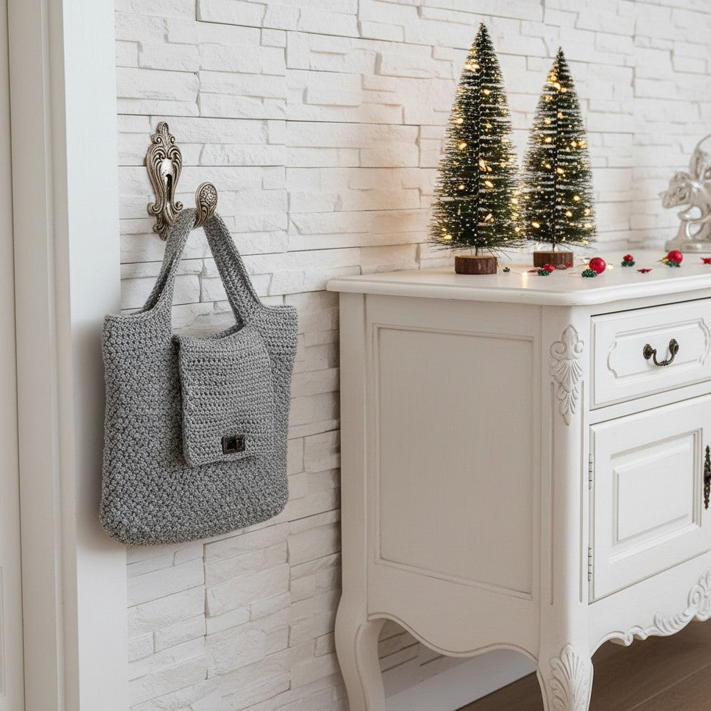 Grey knitted handbag hanging on a wall hook next to a white cabinet with decorative Christmas trees.