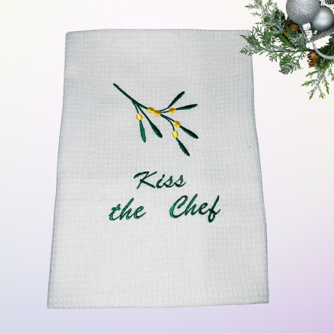 Image of a Christmas related tea towel with embroidered mistletoe and the words kiss the chef