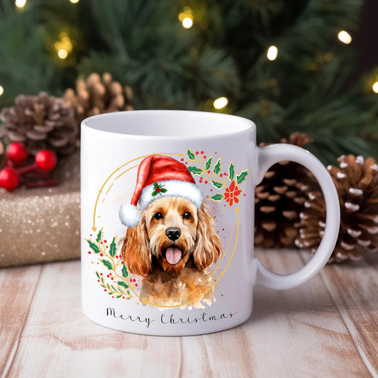A ceramic mug with a watercolour design featuring a Cockapoo dog wearing a Santa hat, positioned in front of a Christmas tree and gifts.