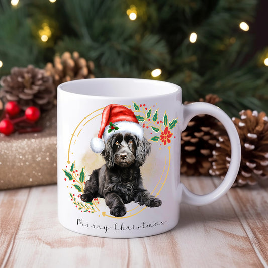 White ceramic mug featuring a Black Cockapoo wearing a Santa Hat positioned in front of a Christmas tree and pine cones.