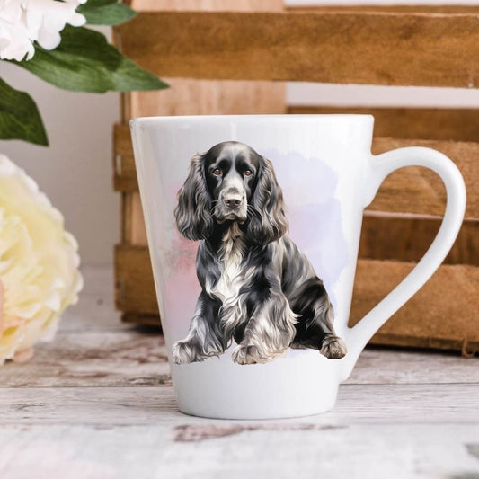 A ceramic latte mug with a printed image of a Cocker Spaniel dog on the side, placed on a wooden surface with a floral pattern and a book in the background.