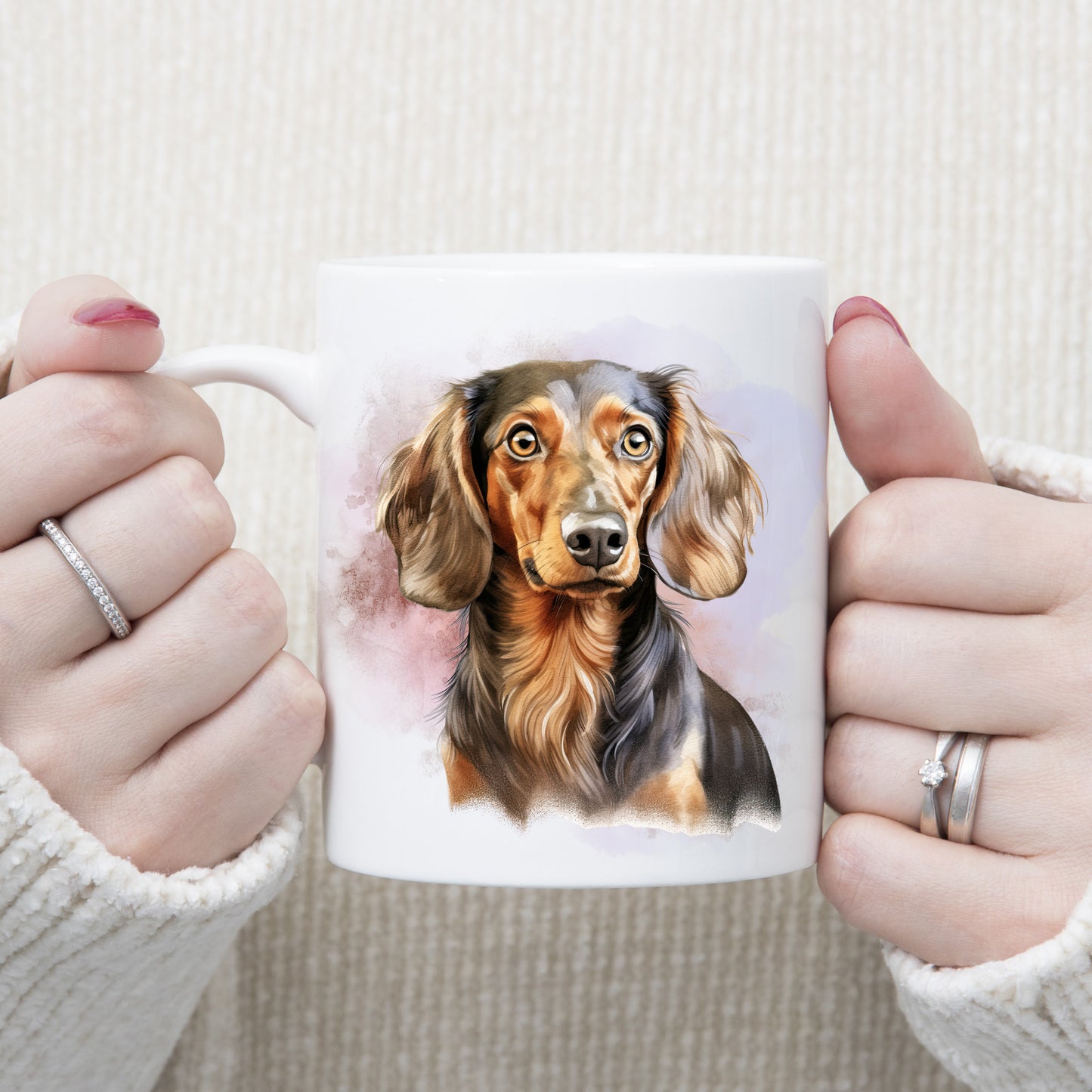 A head and shoulder image of a Chocolate and Tan Dachshund with a pink and lilac smoky background on a  white ceramic mug. A woman is holding the mug with both hands.