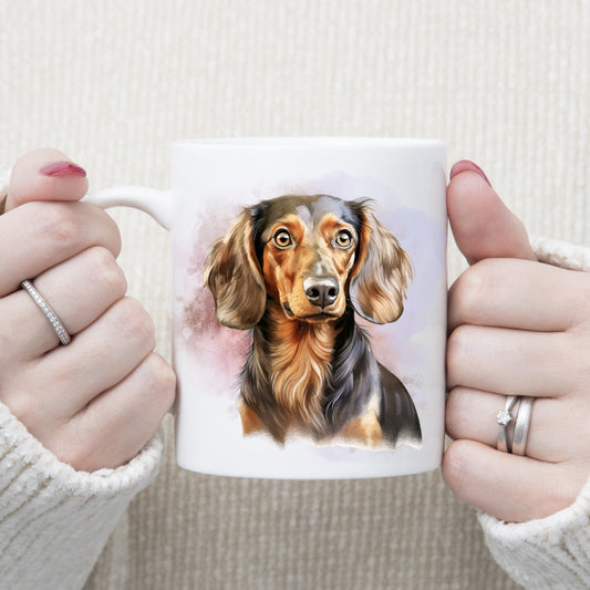 A head and shoulder image of a Chocolate and Tan Dachshund with a pink and lilac smoky background on a white ceramic mug. A woman is holding the mug with both hands.
