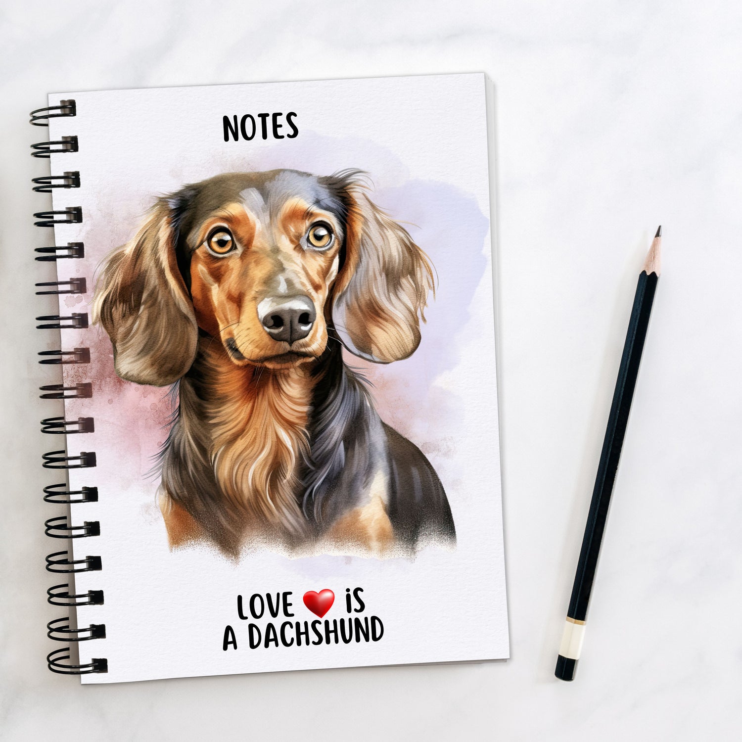 A5 white spiral bound notebook with a liver and tan Dachshund on the front.  Black wire binding and a black pencil to the right hand side.  A quote with a red heart is placed at the bottom of the book.