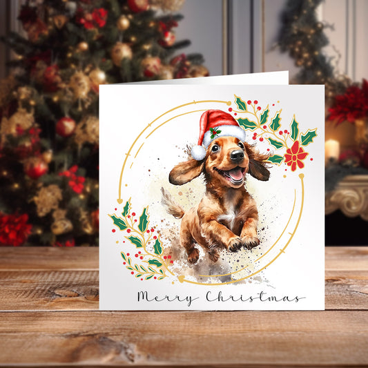 Dachshund wearing a Santa hat on a Christmas themed card. Positioned on a wooden surface with a decorated Christmas tree behind.