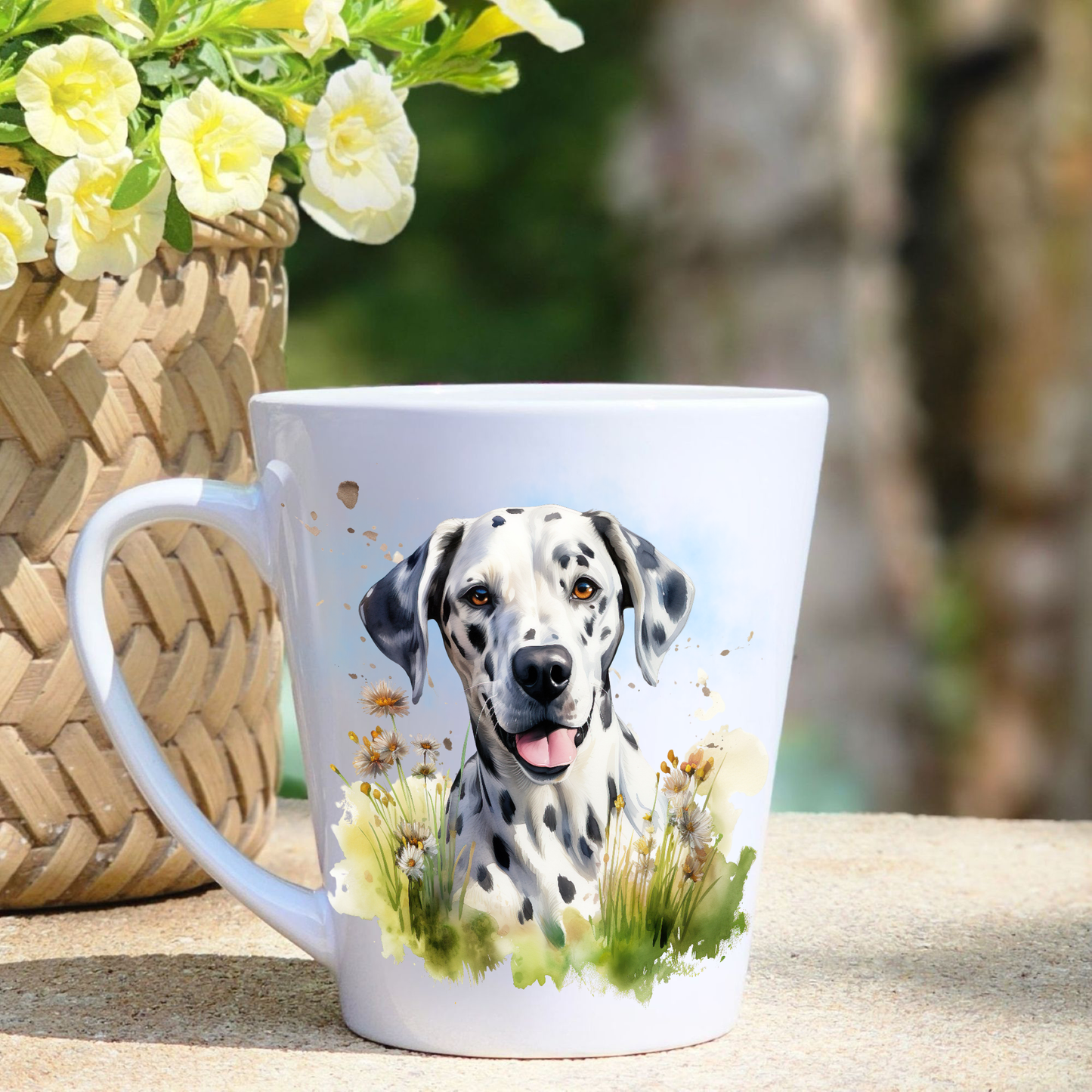 A white ceramic latte mug featuring a Dalmatian sat among grass and wildflowers.  A basket containing yellow flowers sits to the left-hand side.