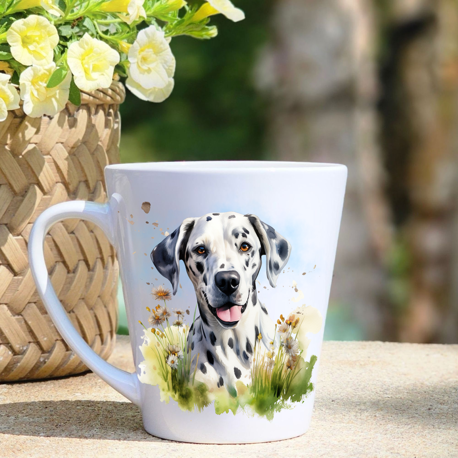 A white ceramic latte mug featuring a Dalmatian sat among grass and wildflowers.  A basket containing yellow flowers sits to the left-hand side.