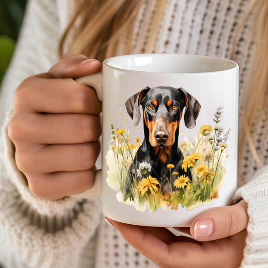A 12oz white ceramic mug with a printed image of a black and tan Doberman facing forward and sitting among yellow flowers. A computer keyboard sits in the background.  The mug is positioned on a wooden surface.