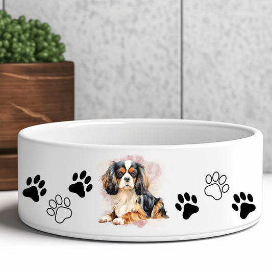 Cavalier King Charles Spaniel tri-colour pet bowl. Image with the dog in a lying position.  Black and white paw prints decorate the bowl.