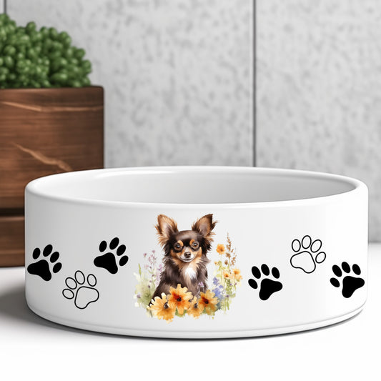 Chocolate and tan long haired chihuahua sitting among flowers on a dog bowl.