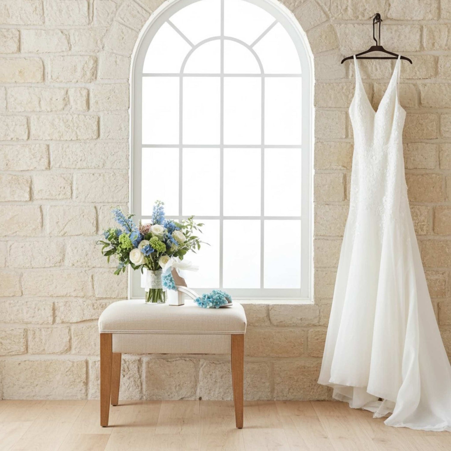 Blue floral bridal shoe on a beige stool with bridal gown hung by the side and bridal bouquet.