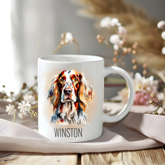 An English Setter coffee mug personalised with a pet name. The mug is sat on a wooden surface with a creamy coloured cloth and various flowers adorn the background.