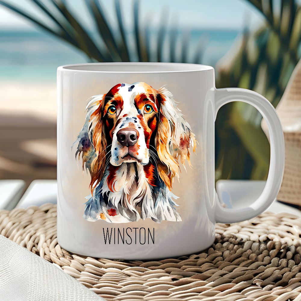 White ceramic mug showing an English Setter on a light smoky effect background.  Mug is placed on a wicker mat  and a seascape is seen behind a large palm frond.