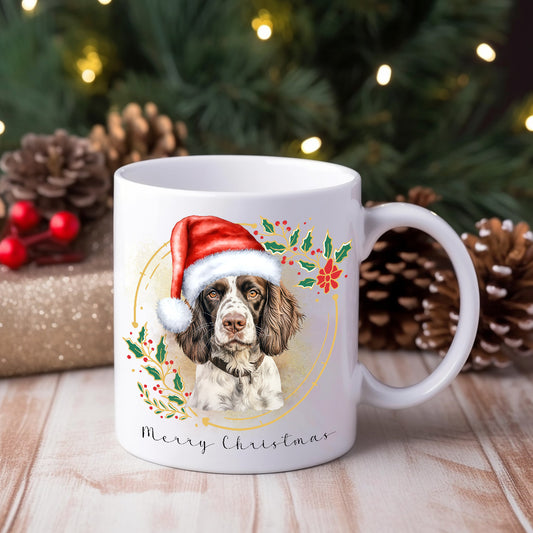 A white ceramic mug with a watercolour design of an English Springer Spaniel wearing a Santa hat, placed on a wooden surface with Christmas decorations around.