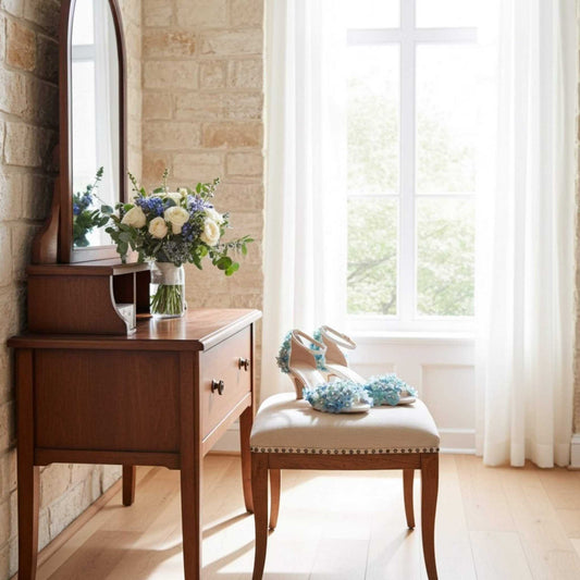 Wooden vanity with mirror, flowers, and a chair with blue kitten heel bridal shoes on a stone wall background.