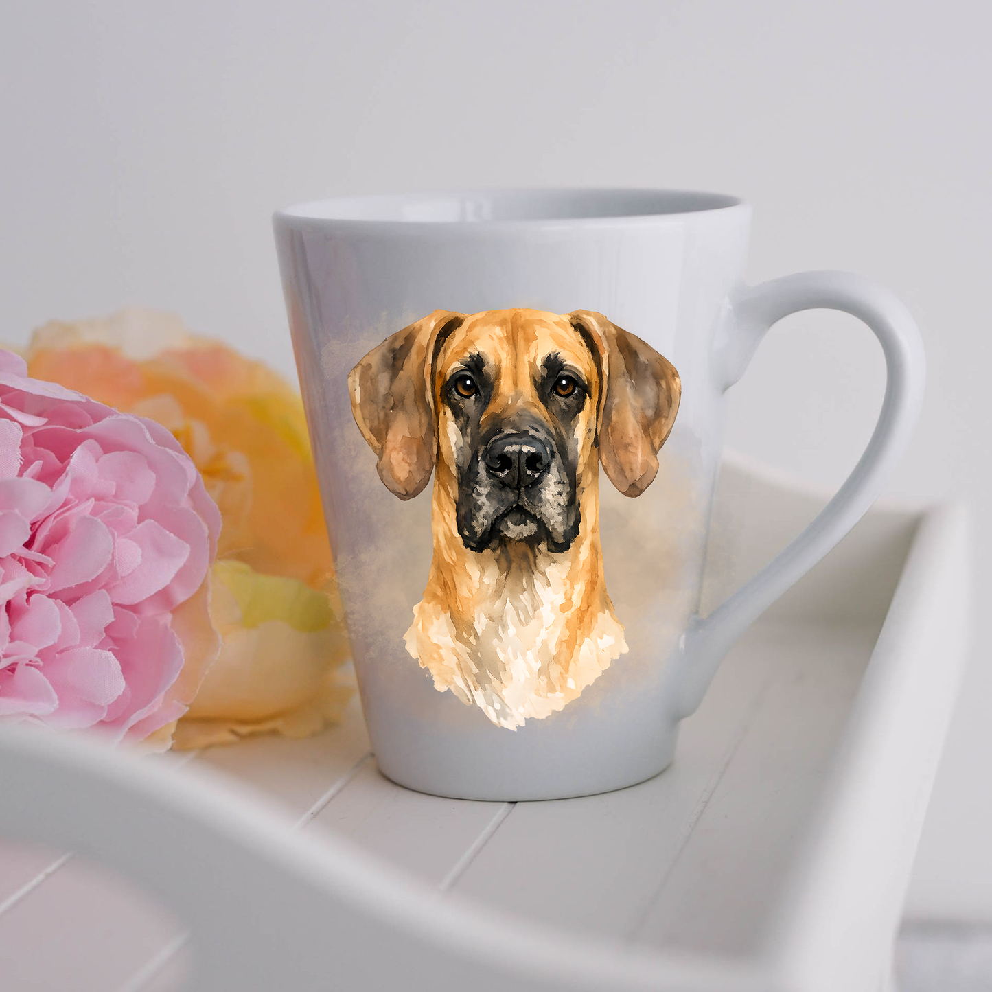 A Fawn Great Dane is shown on a white ceramic latte mug in a smoky background and looking forward.  The mug is placed on a white tray with pink and yellow flowers. 