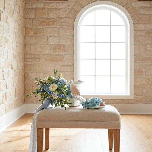 Bouquet of flowers and wedding shoes on a stool in a room with stone walls and a large window.
