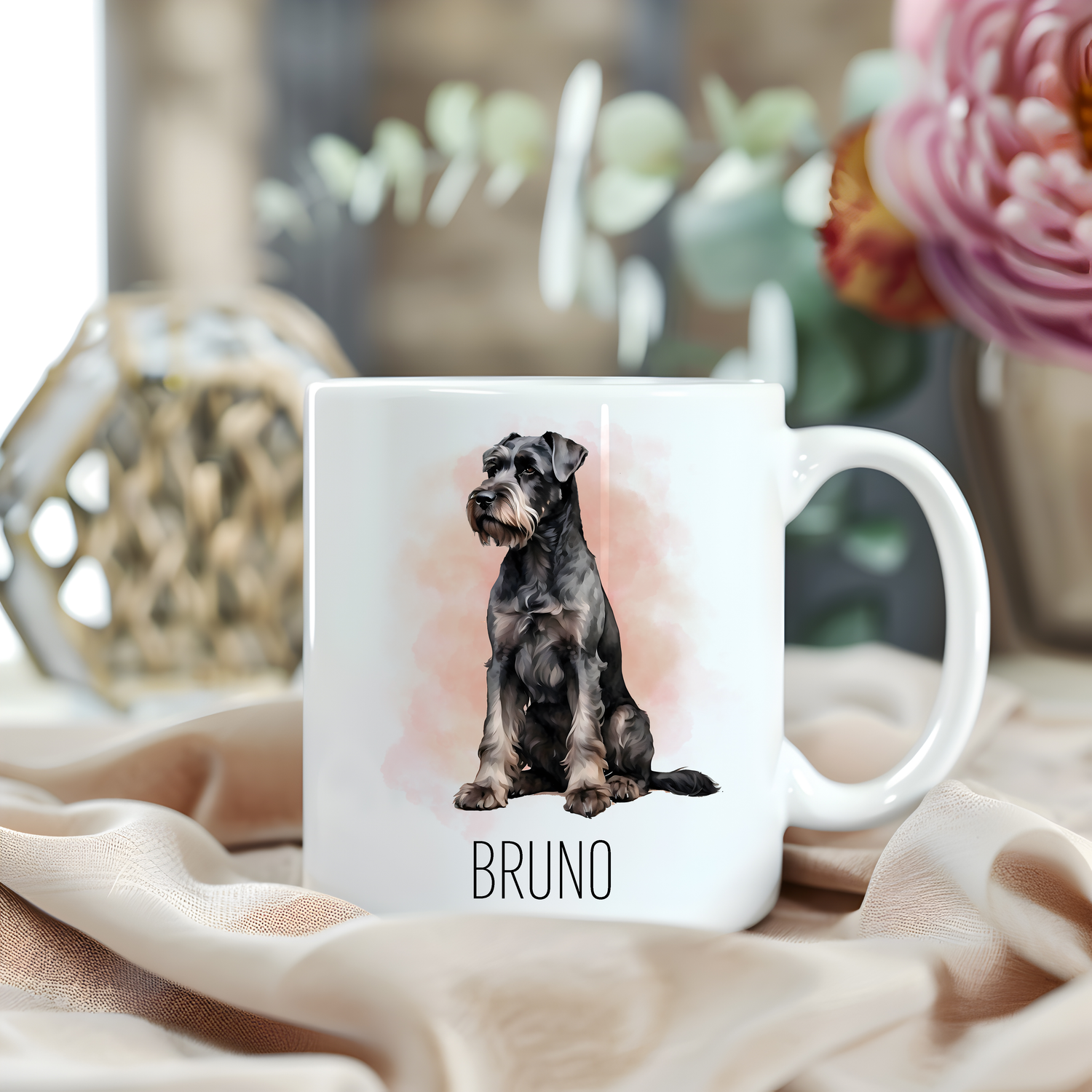 A Giant Schnauzer is sitting on a white personalised ceramic mug which has been placed on a beige cloth.  A large pink flower with green foliage accessorizes the image.