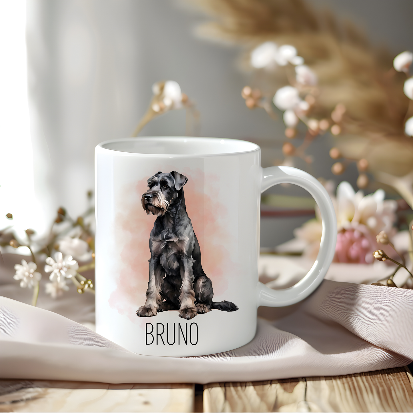 A lovely Giant Schnauzer coffee mug that is personalised with a pet name.  The mug is sat on a wooden surface with a creamy coloured cloth and a variety of flowers decorate the background.