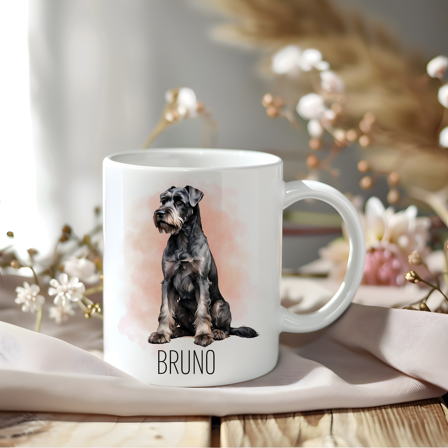 A lovely Giant Schnauzer coffee mug that is personalised with a pet name.  The mug is sat on a wooden surface with a creamy coloured cloth and a variety of flowers decorate the background.
