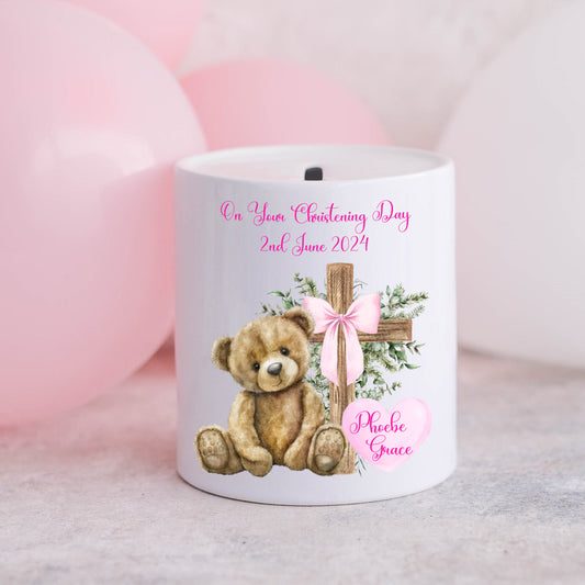 Personalised christening money box for a girl. Teddy and cross with a pink ribbon and pink balloons in the background.