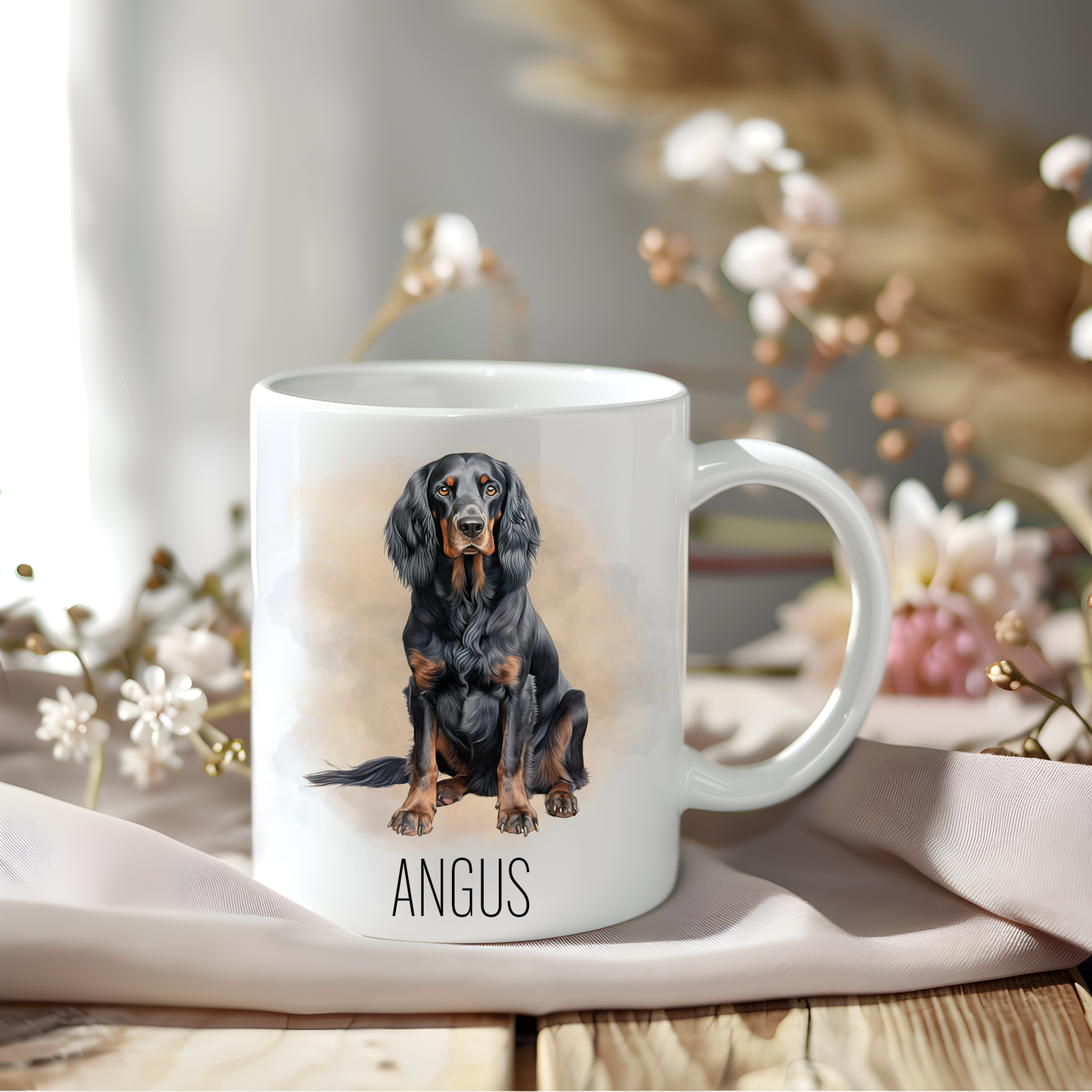 Gordon Setter coffee mug personalised with a pet name.  The mug is sat on a wooden surface with a creamy coloured cloth and various flowers adorn the background.