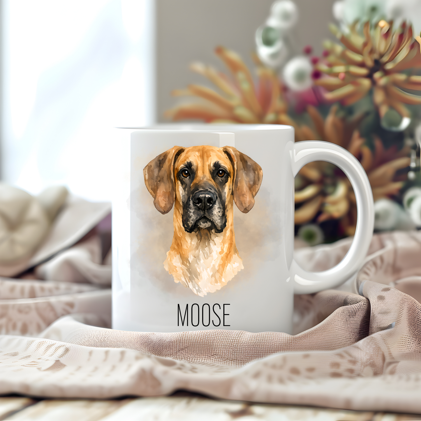 Personalised coffee mug featuring a Fawn Great Dane on a white ceramic mug which has been placed on a beige cloth.  Stems of large  flowers accessorizes the image.