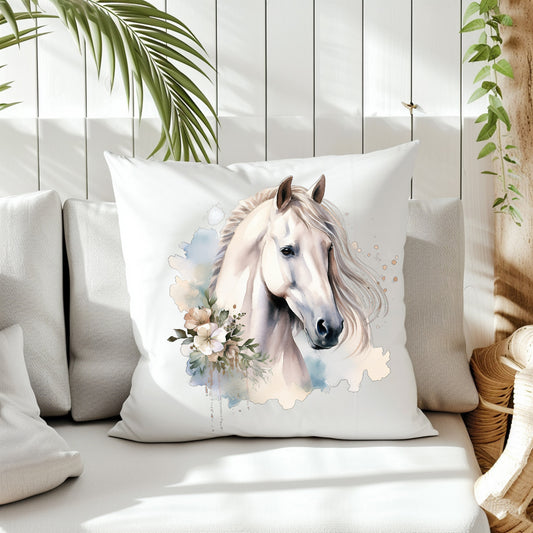 A white horse head and white flowers decorate the front of a white cushion which is placed on a cream sofa.  White panels and green fern create the background.