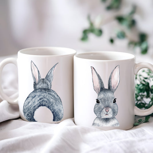 Two white ceramic mugs with watercolor illustrations of rabbits, one showing the rabbit from the front and the other from the back.