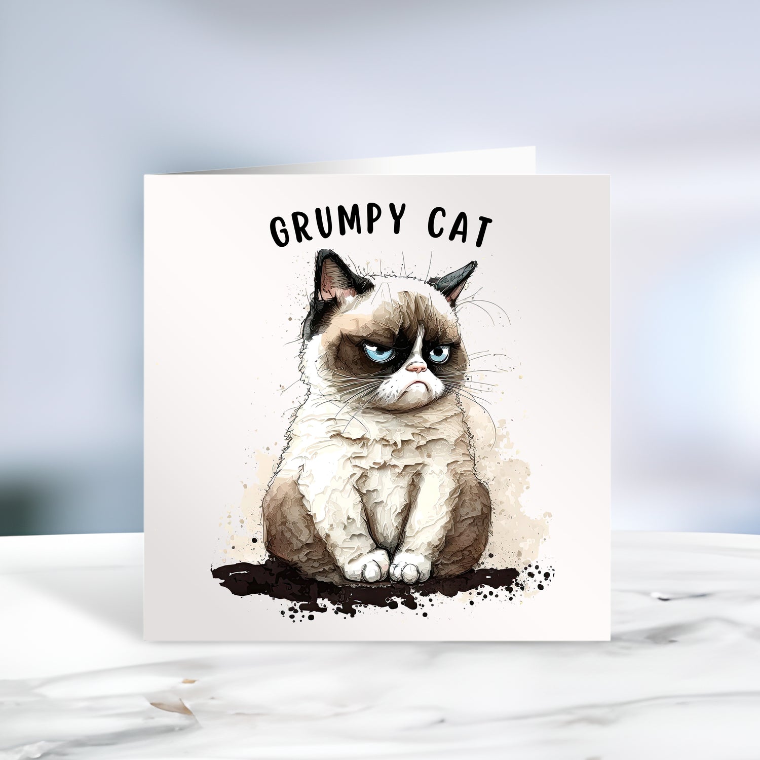 Grumpy cat with blue eyes and dark markings to the ears and around the eyes.  The cat is on a white card and the words Grumpy Cat at the top of the card.  The card is placed on a grey marble surface.