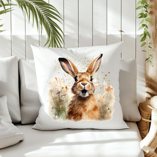 A Spring Hare stands chest high in grass wild flowers and splashes in the background on the front of a white cushion which is placed on a cream sofa.  White panels and green fern create the background.