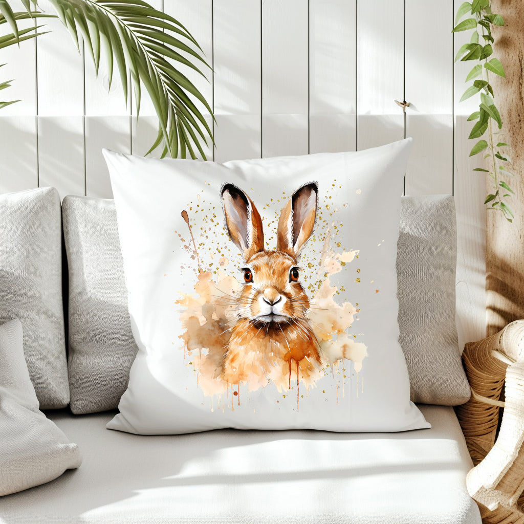A brown Hare head and shoulders image with a splattered and smoky background on the front of a white cushion which is placed on a cream sofa.  White panels and green fern create the background.