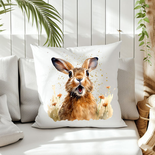 A Spring Hare with a smiley expression on a splattered background and small orange flowers decorate the front of a white cushion which is placed on a cream sofa. White panels and green fern create the background.