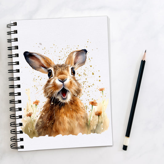 White notebook with spiral bindng. A brown hare with a surprised expression is facing forward on a speckled background with orange flowers. A pencil is laid to the right hand side.
