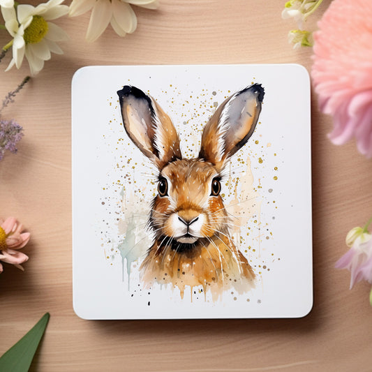 Brown hare looking forward on a white coaster placed on a wooden surface and flowers around the edges.
