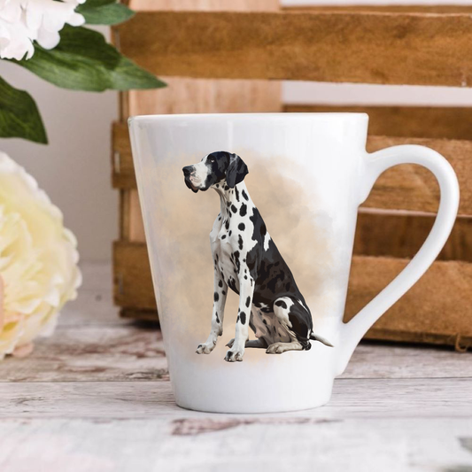 A white ceramic latte mug stands on a wooden surface with a crate in the background. The mug features a Harlequin Great Dane. A large yellow flower peeps in from the left-hand side.