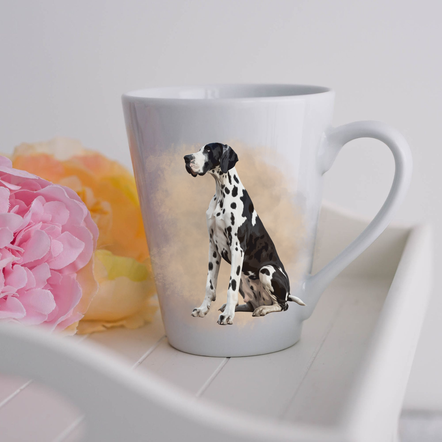 A Harlequin Great Dane is sitting on a white ceramic latte mug in a smoky background and looking forward.  The mug is placed on a white tray with pink and yellow flowers. 