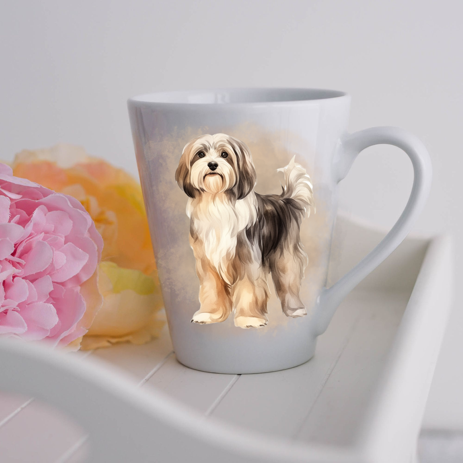 A Havanese dog is shown stood on a white ceramic latte mug in a smoky background and looking forward.  The mug is placed on a white tray with pink and yellow flowers. 
