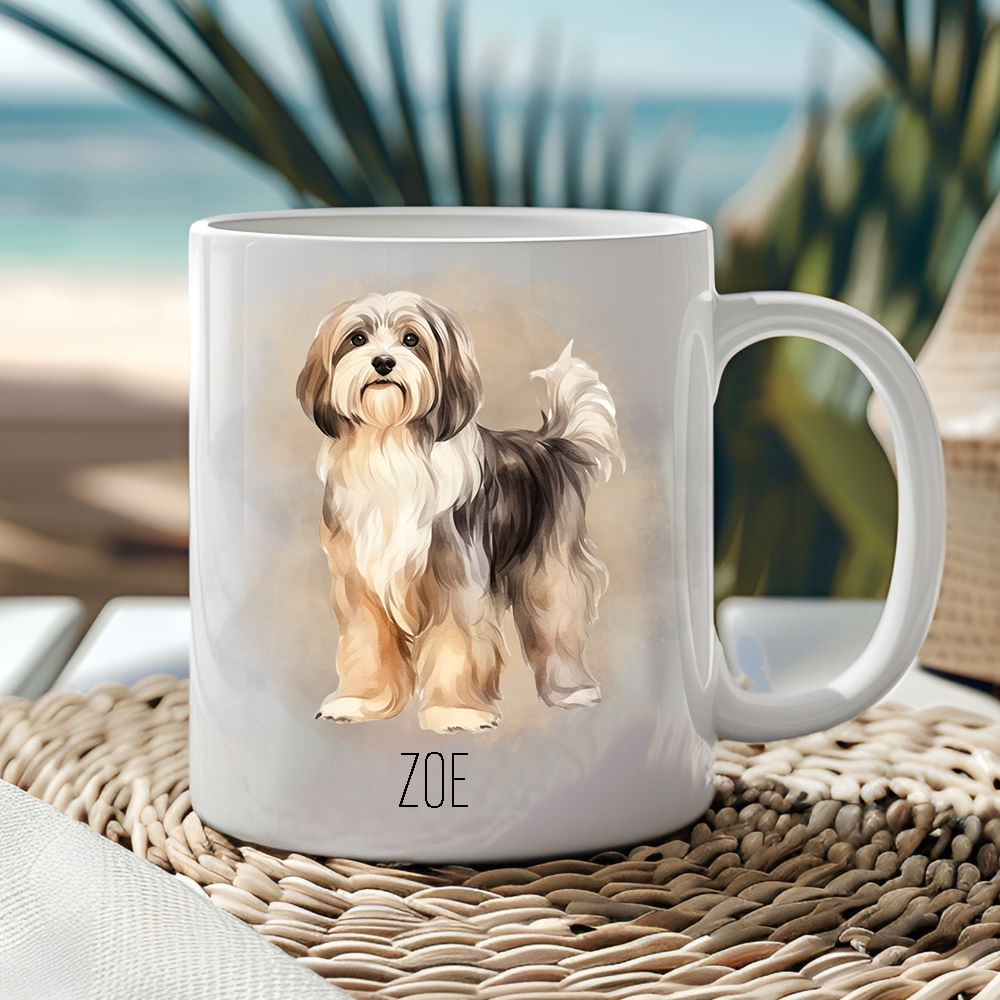This white ceramic mug shows a Havanese dog standing among a gold coloured smoke effect background.  The mug is placed on a wicker mat  with a sea scene behind.